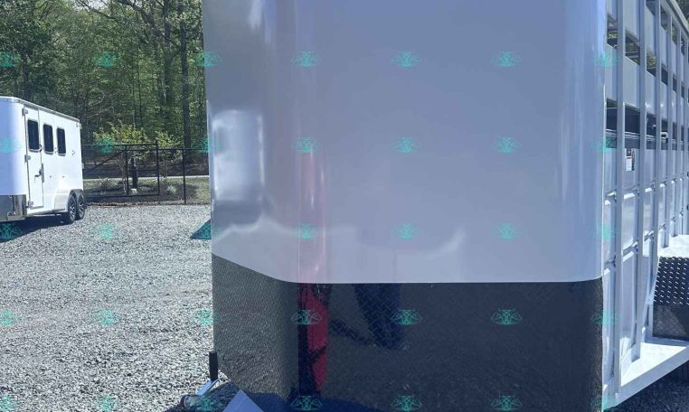 White livestock trailer with front diamond-plate rock guard and hitch in a gravel lot; Valley Trailers logo on side; another trailer in background