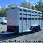 White two-axle livestock trailer with side vents and divider gates on a gravel lot, ready for transport.