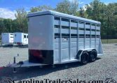 White two-axle livestock trailer with side vents and divider gates on a gravel lot, ready for transport.