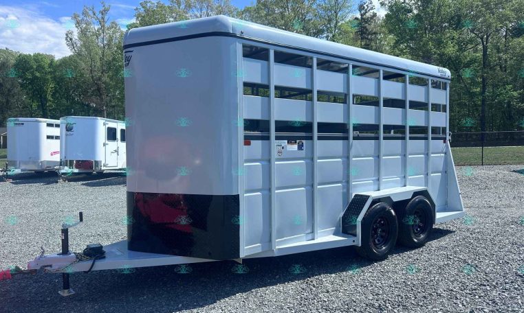 White two-axle livestock trailer with side vents and divider gates on a gravel lot, ready for transport.