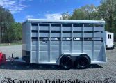 White tandem-axle livestock trailer on a gravel lot with trees in the background; CarolinaTrailerSales watermark at bottom.