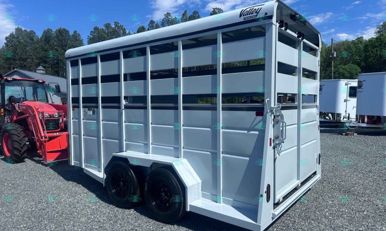 White livestock trailer with two axles and open side panels on a gravel lot, next to a red tractor, under a blue sky, branding reads Valley Trailers (CarolinaTrailerSales watermark).