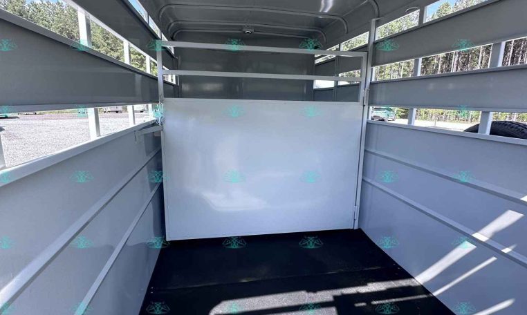 Interior of an empty light-gray trailer with a divider at the far end, ribbed side panels, and a black floor under daylight from side openings.