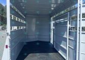Interior of an empty gray horse trailer with divider stalls on the sides and open rear doors, showing a black rubber floor and a clear blue sky outside.