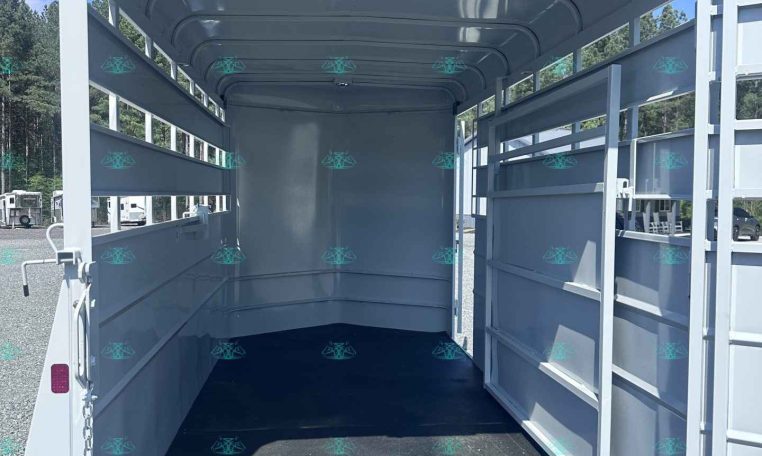 Interior of an empty gray horse trailer with divider stalls on the sides and open rear doors, showing a black rubber floor and a clear blue sky outside.