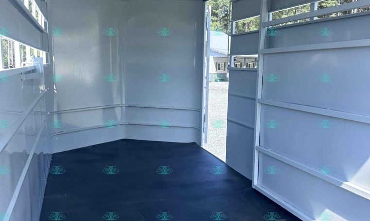 Interior of an empty white horse trailer with a black rubber floor and open back ramp, daylight outside visible