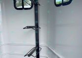 Interior of a cargo trailer with a vertical support post and two fold-down brackets for securing gear, plus two rectangular windows in the side walls.