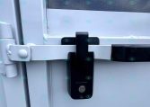 Trailer door with a black locking latch securing a horizontal white bar across the door.