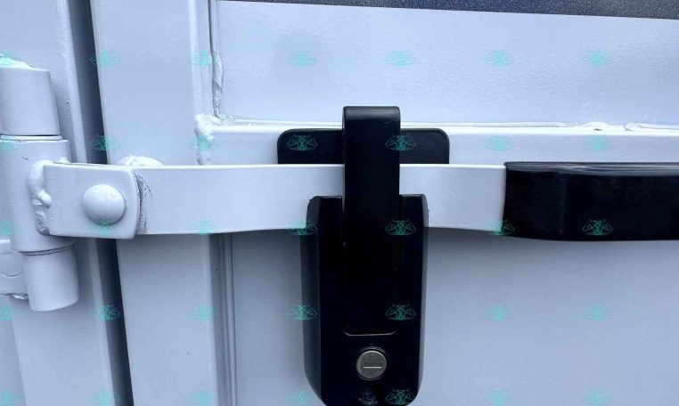 Trailer door with a black locking latch securing a horizontal white bar across the door.