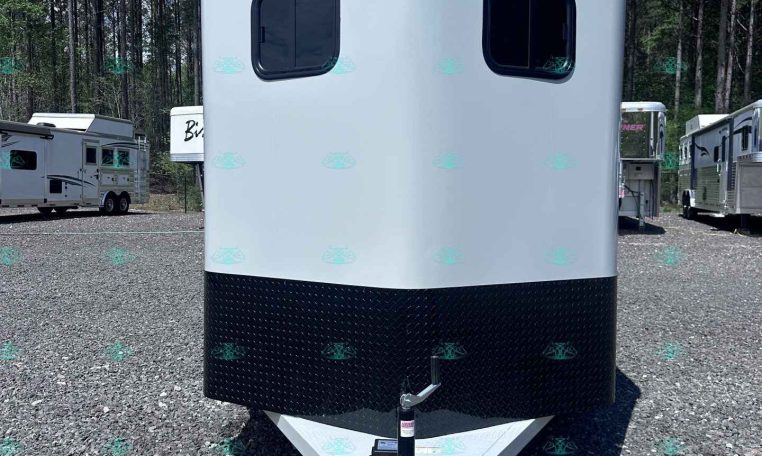 White Valle trailer with a black diamond-plate lower section sits on a gravel lot, hitch facing viewer, trees in background.