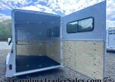 Open horse trailer with rear and side doors open, showing plywood interior walls and a non-slip black floor on a gravel lot.