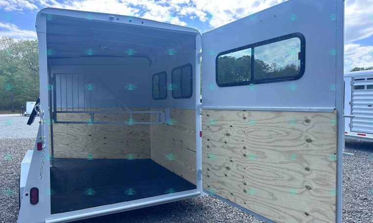 Open horse trailer with rear and side doors open, showing plywood interior walls and a non-slip black floor on a gravel lot.