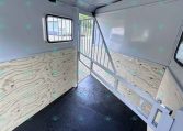 Interior of a light-gray horse trailer with a divider, plywood side walls, small window, and a rubber/non-slip floor