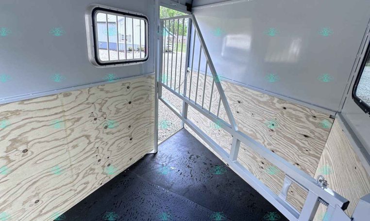 Interior of a light-gray horse trailer with a divider, plywood side walls, small window, and a rubber/non-slip floor
