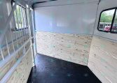 Interior of a empty horse trailer with plywood sides, black rubber floor, and a metal divider on the left, ready for loading animals