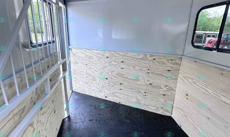 Interior of a empty horse trailer with plywood sides, black rubber floor, and a metal divider on the left, ready for loading animals