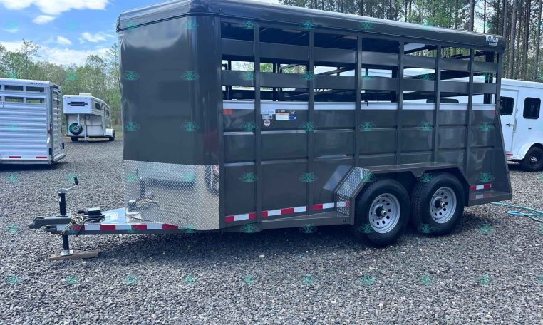 Grey two-axle livestock trailer with slatted sides and diamond-plate front, parked on gravel (carrying branding for CarolinaTrailerSales.com).