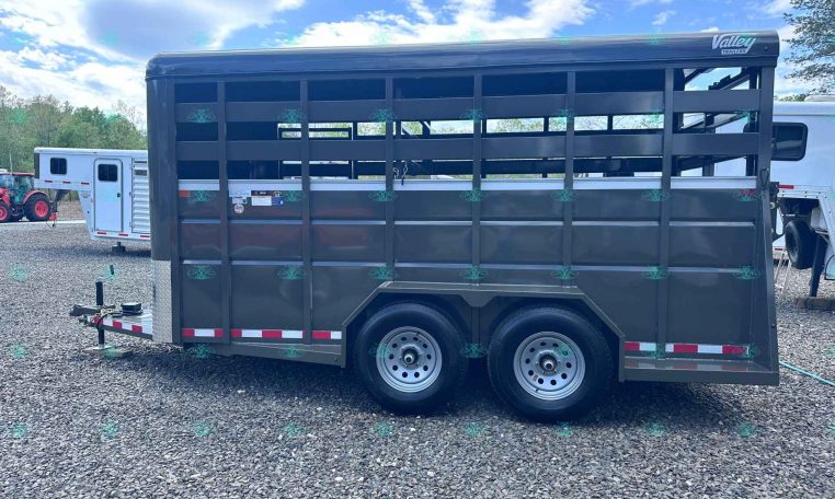 Two-axle black livestock trailer with open side slats and a gooseneck hitch, branding 'Valley Trailers', on a gravel lot