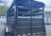 Rear view of a dark gray livestock trailer with its ramp down on a gravel lot.