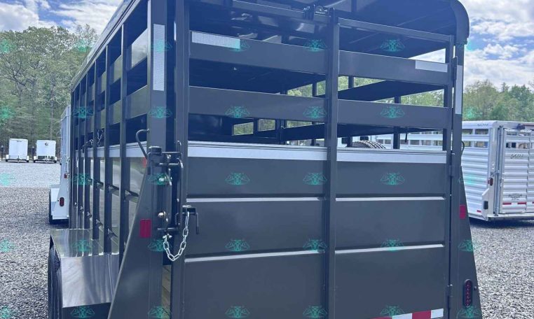 Rear view of a dark gray livestock trailer with its ramp down on a gravel lot.