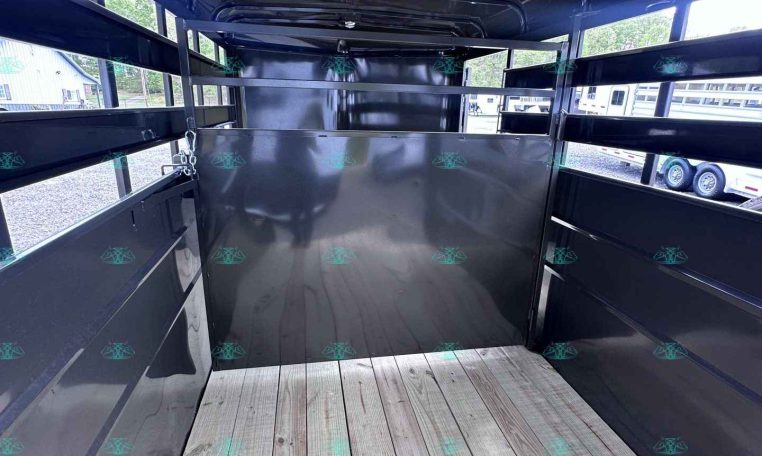 Interior of a black trailer with a wooden plank floor and metal side walls; an internal divider at the far end, empty and ready for cargo.