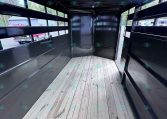 Interior of an empty black trailer with a wooden plank floor and open rear doors, viewed from inside the long narrow space.