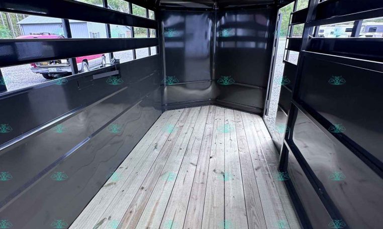 Interior of an empty black trailer with a wooden plank floor and open rear doors, viewed from inside the long narrow space.