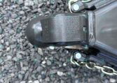 Close-up of a trailer hitch coupler on a gravel surface with safety chains attached nearby.