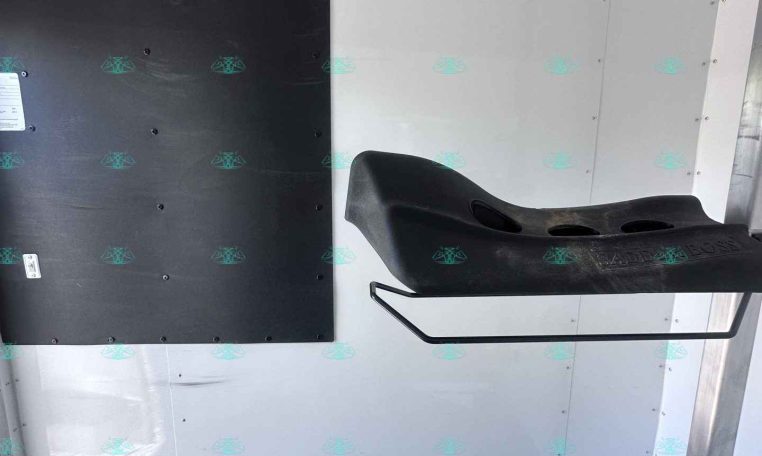 Interior of a trailer cargo area showing a black wall panel with multiple metal hooks and a curved black step seat mounted to the right side.