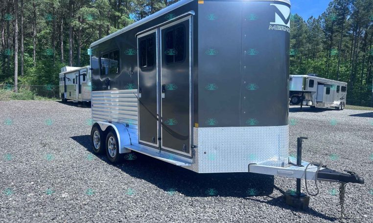 Silver travel trailer on a gravel lot with trees in the background and a second trailer in the distance.
