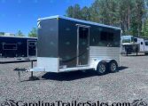 Dark gray tandem-axle trailer on a gravel lot, with trees in the background under a clear blue sky.