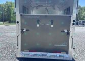 Rear of a Merhow horse trailer with doors open, showing empty stalls inside on a gravel lot outside under a blue sky.