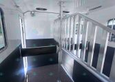 Interior of a white horse trailer with a vertical metal divider and black padded benches along both walls of the trailer's aisle