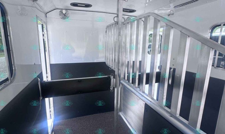Interior of a white horse trailer with a vertical metal divider and black padded benches along both walls of the trailer's aisle