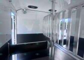 Interior of a horse trailer with a metal vertical divider and a dark non-slip floor, ventilation fan, and light entering from side windows