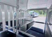 Interior of a metal livestock trailer showing aluminum gates, a ramp, and partitioned stalls viewed from inside.