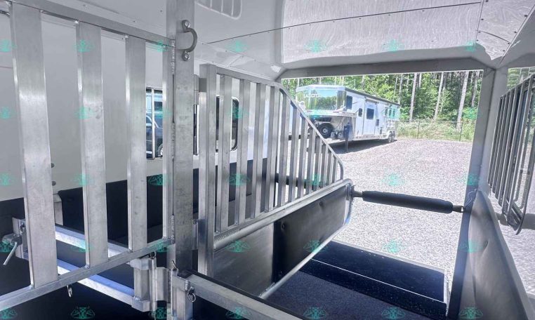 Interior of a metal livestock trailer showing aluminum gates, a ramp, and partitioned stalls viewed from inside.
