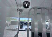 Interior of a light-gray trailer with a metal divider, ceiling vent, and small fan; outside are other trailers.