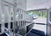 Interior of a metal livestock trailer with aluminum divider gates and a rubberized ramp, seen from the doorway toward an outdoor trailer area