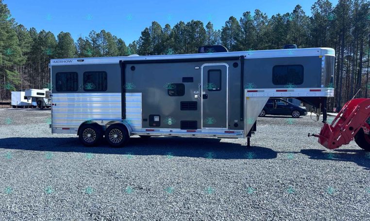 Two‑axle Merhow horse trailer with living quarters, parked on a gravel lot with trees in the background, side door and windows visible