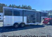 Gray Merhow horse trailer with two axles and side entry door on a gravel lot, with a red tractor nearby in the background.