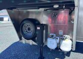 Under-trailer storage area showing a spare tire in the wheel well, a metal utility box, and two connected propane tanks beneath the trailer.