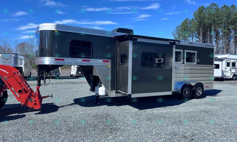 Gooseneck horse trailer with black upper and silver lower panels on a gravel lot, trees in the background.