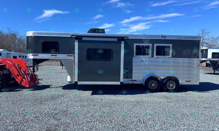 Merhow horse trailer with gray and silver siding, two windows, and tandem wheels parked on a gravel lot beside a red tractor attachment.
