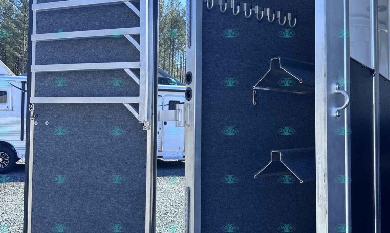 Open trailer interior with wall of gear hooks and a small drawer containing a coiled hose at the door.