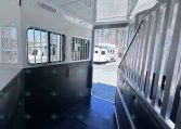 Interior of a white horse trailer with black padded walls and metal stalls, doorway open to bright outside light.