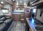Interior of a modern RV living area with a leather couch, kitchenette, and stairs to a loft bed above the kitchen area.