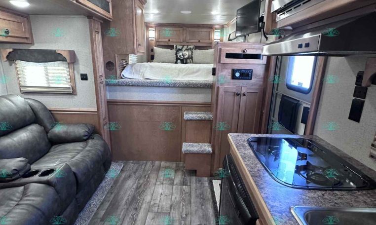 Interior of a modern RV living area with a leather couch, kitchenette, and stairs to a loft bed above the kitchen area.