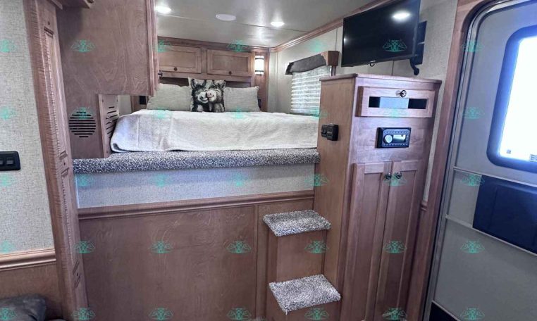 RV bedroom with a raised platform bed, wooden cabinets, and carpeted stairs leading up to the bed