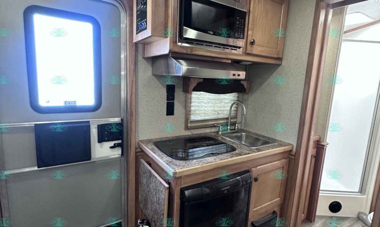 Interior of a compact RV kitchen with microwave above a two-burner stove and sink, and a black mini fridge beside the cabinet.